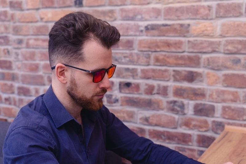 mężczyzna w niebieskiej koszuli mający założone na twarzy okulary blokujące światło niebieskie biohac smart na tle ceglanej ściany