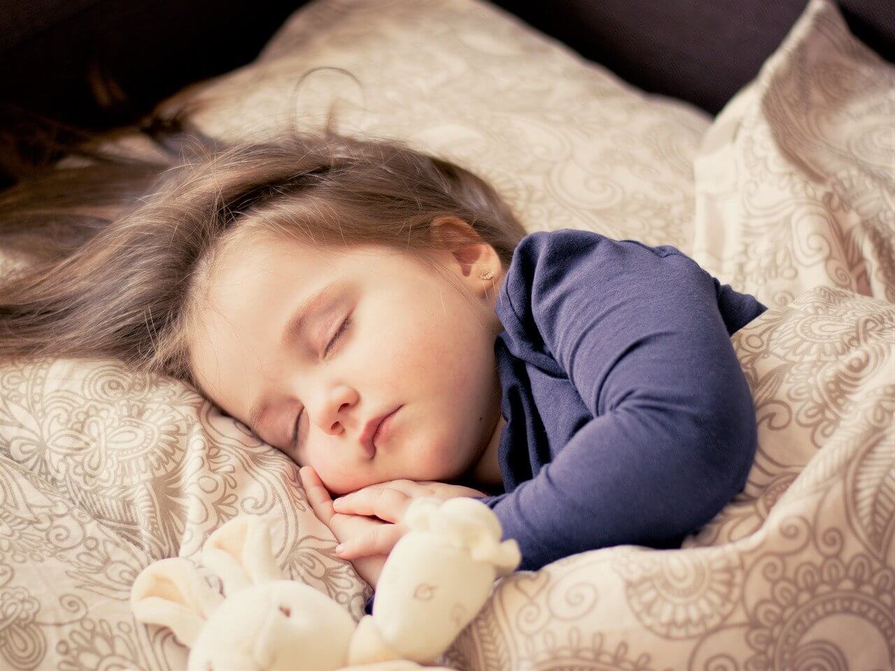 Małe dziecko śpiące bokiem na poduszce z pluszową zabawką. Jak sen wpływa na jej mózg?