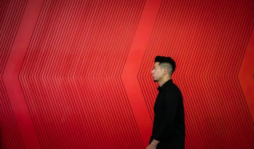 Mężczyzna w czerni stojący bokiem na tle ściany z czerwonym światłem